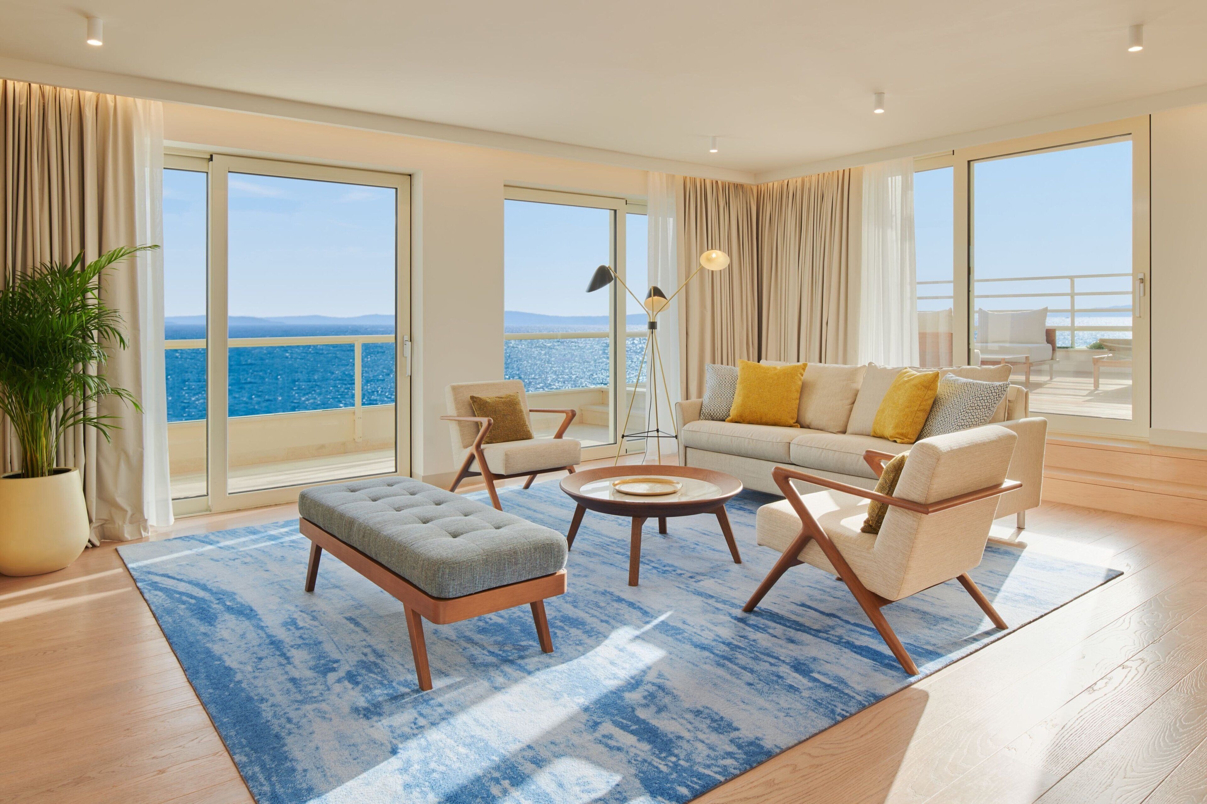Un salón amplio con un ventanal que ofrece vistas al mar, un sofá con cojines amarillos y una mesa de centro redonda.