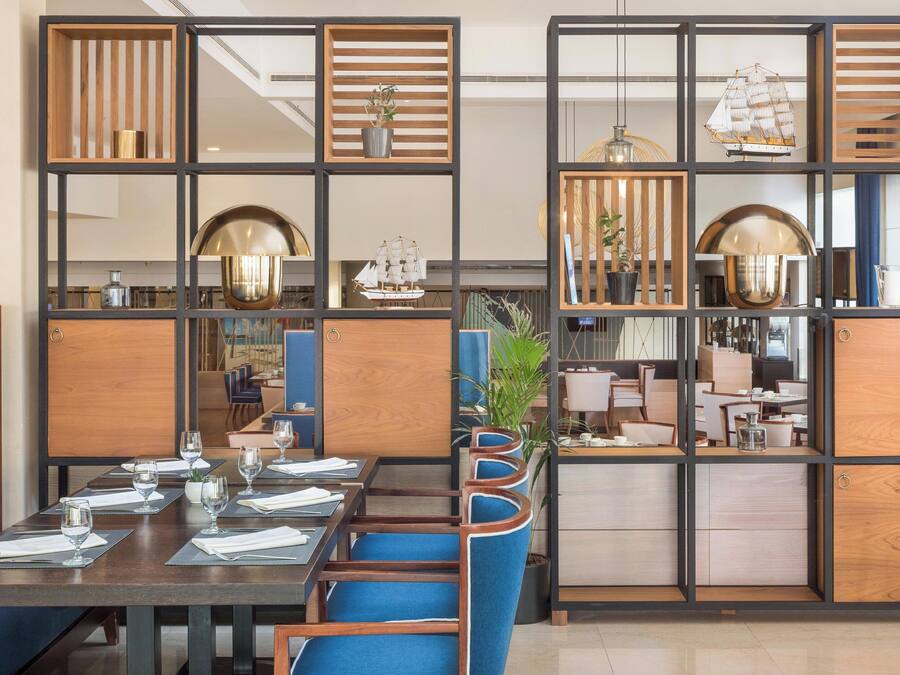Un restaurante con una decoración moderna, que presenta separadores de madera, sillas tapizadas en azul y diferentes tipos de mesas.