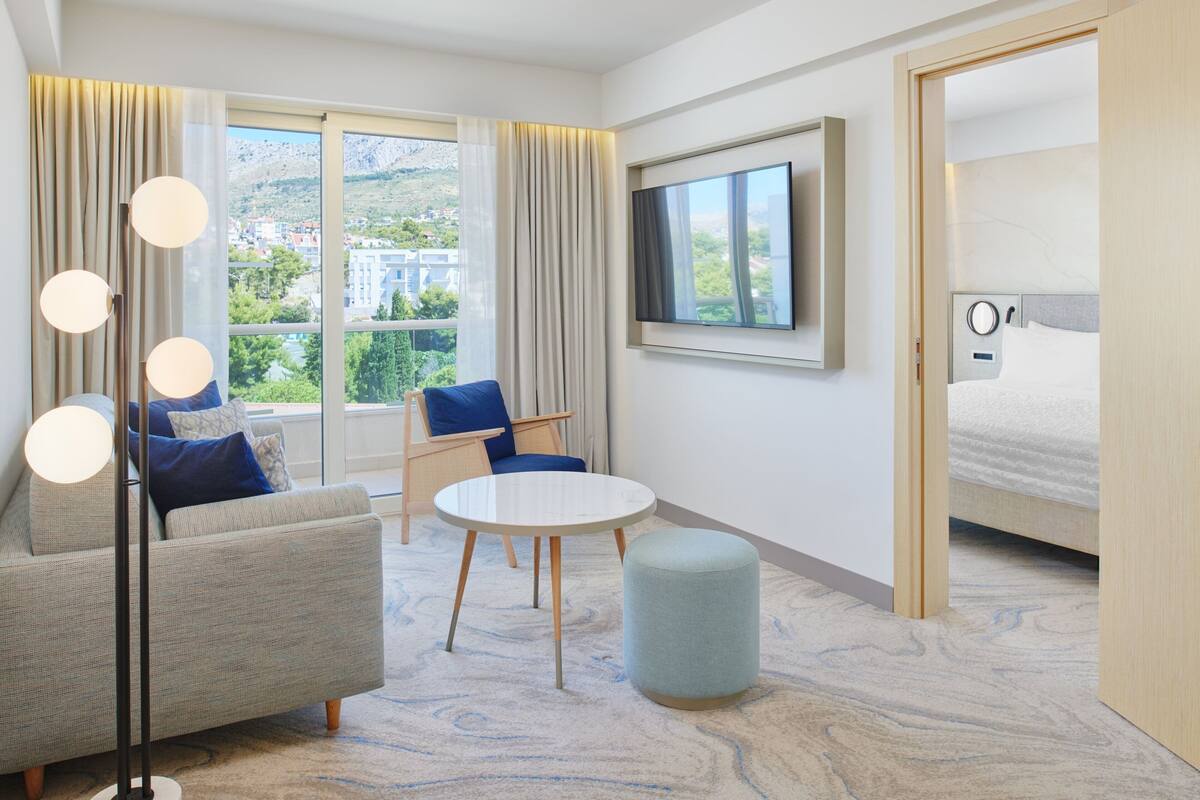 A modern hotel room with a sofa, a round table, a TV, and a bed.