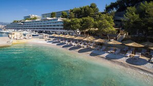 Un hotel frente a la playa con aguas turquesas cristalinas, sillas de sol y sombrillas.