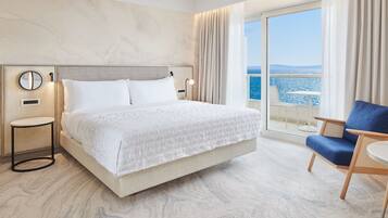 Habitación de hotel con una cama grande, una silla, una mesita de noche y vista al mar.