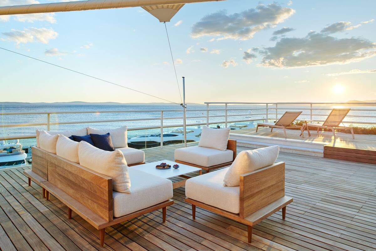 A wooden deck with a sofa and chairs facing a body of water.