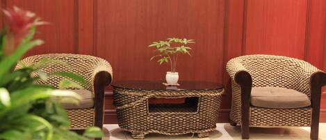 A room with two wicker chairs, a round wooden table with a vase and a plant, and a red wall.