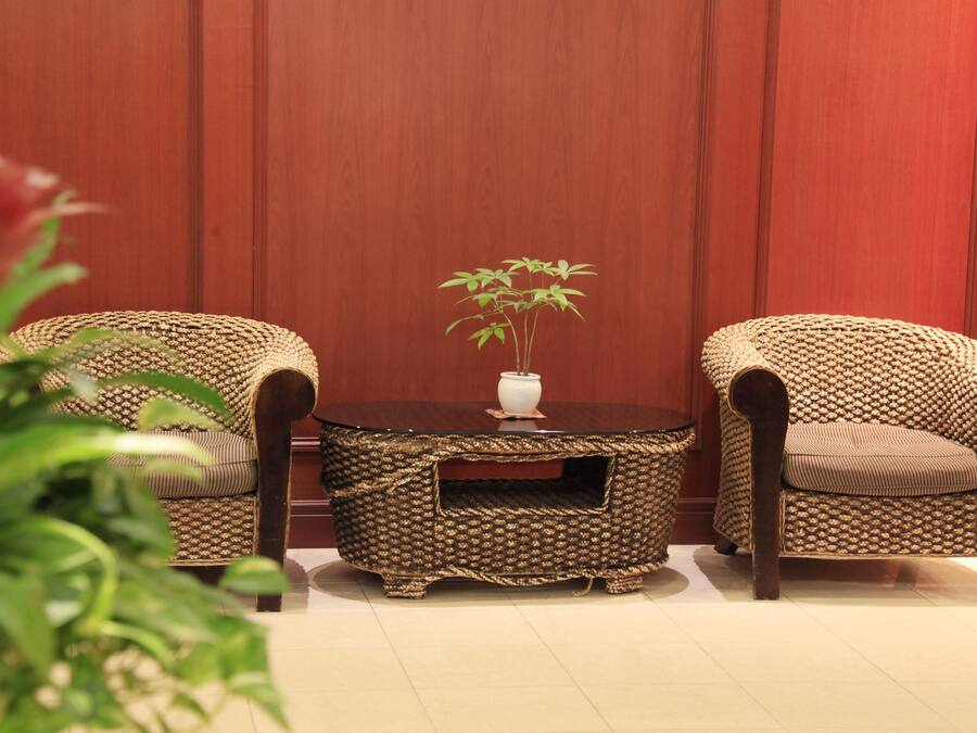 A room with two wicker chairs, a round wooden table with a vase and a plant, and a red wall.