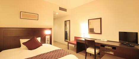Habitación de hotel con cama, escritorio, silla, televisión y espejo.