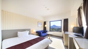 A hotel room with a large bed, a desk with a TV, a small table with a lamp, and a window with a view of mountains. - Quintessa Hotel Sasebo (Sasebo)
