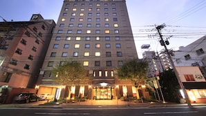 A multi-story hotel with a prominent entrance, a parking area, and a visible sign for the hotel. - Quintessa Hotel Sasebo (Sasebo)