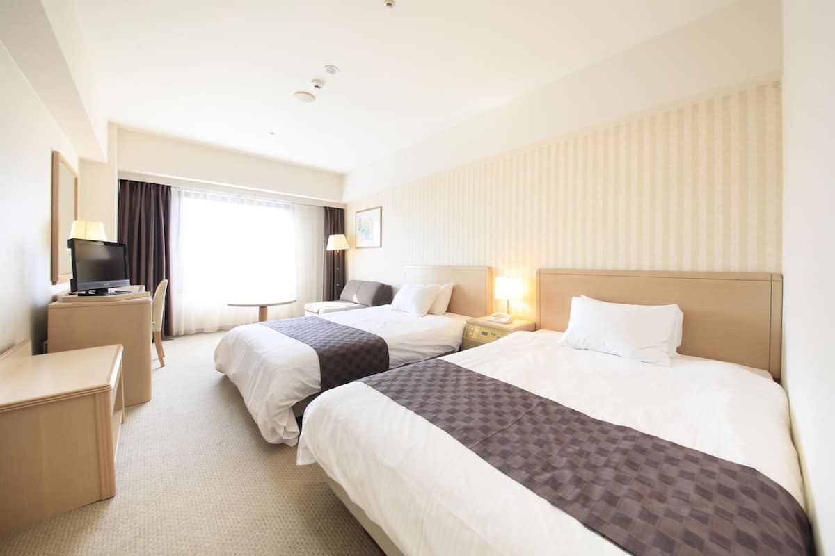 A hotel room with two beds, a desk, a chair, a television, and a window with curtains.