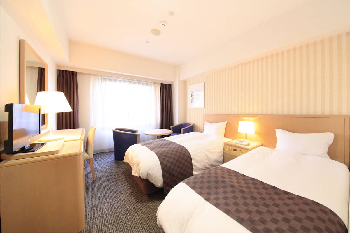 A hotel room with two beds, a desk with a computer, a chair, a small table, and a lamp.
