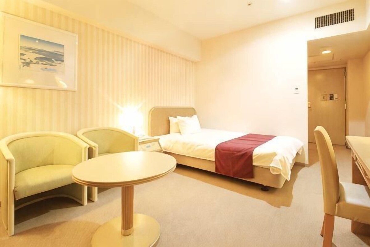 Una habitación de hotel con cama, dos sillones, una mesita redonda y una mesita de noche.