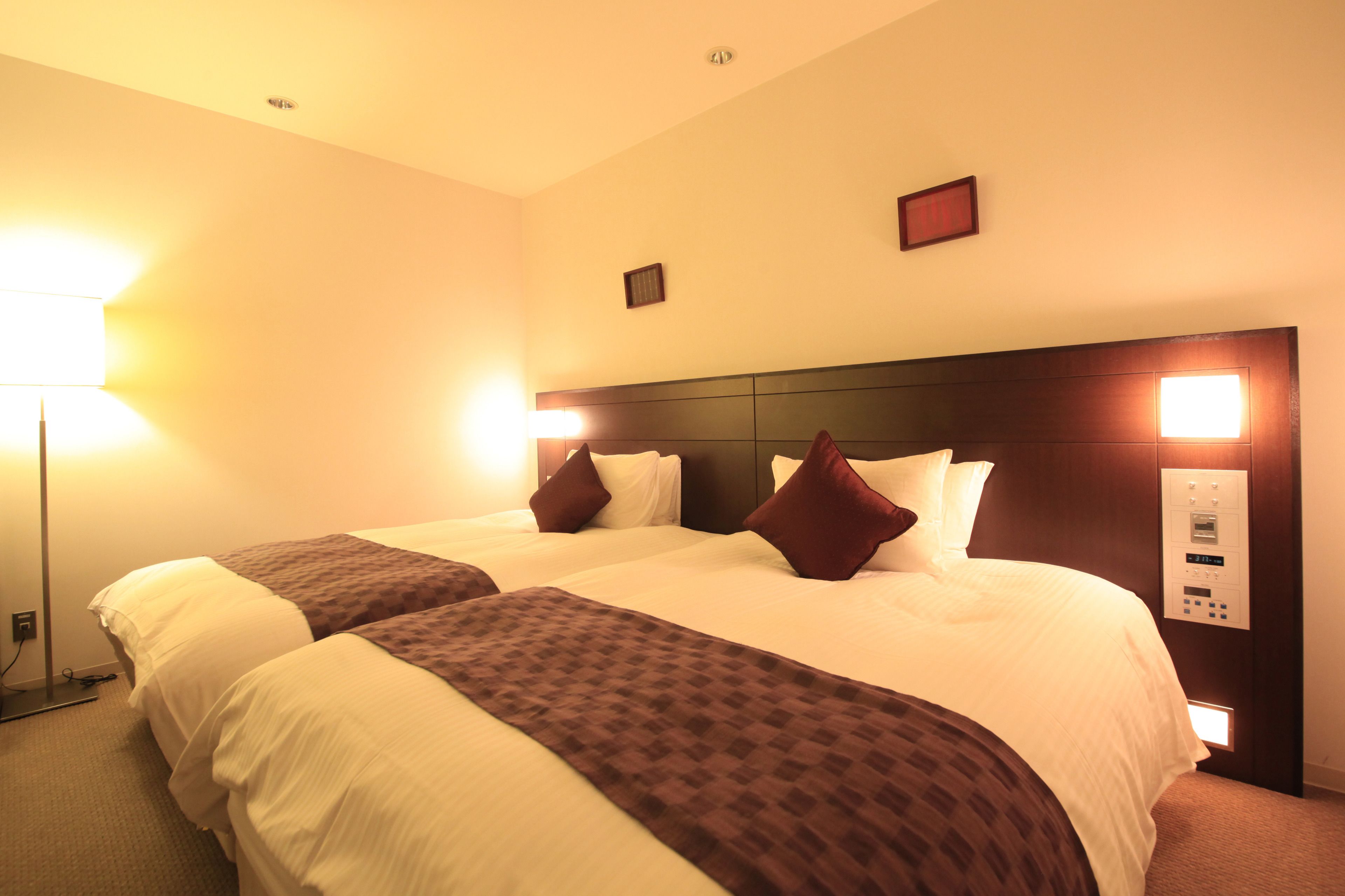 Habitación de hotel con dos camas, cabecera con controles integrados y mesita de noche.
