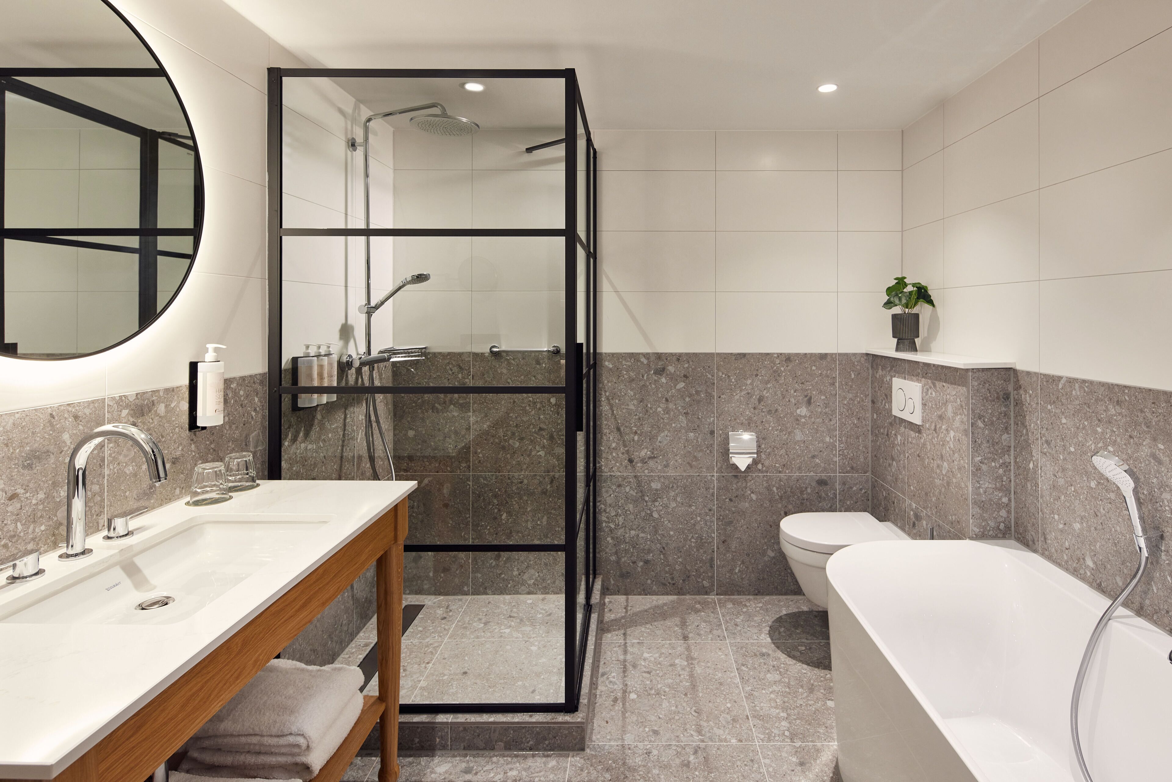 A modern bathroom with a glass shower enclosure, a freestanding bathtub, and a vanity with a mirror and sink.