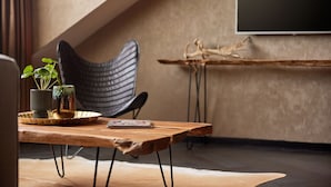 Ein modernes Zimmer mit einem Holztisch, einem schwarzen Stuhl, einer Topfpflanze und einem flachbildfernseher an der Wand.
