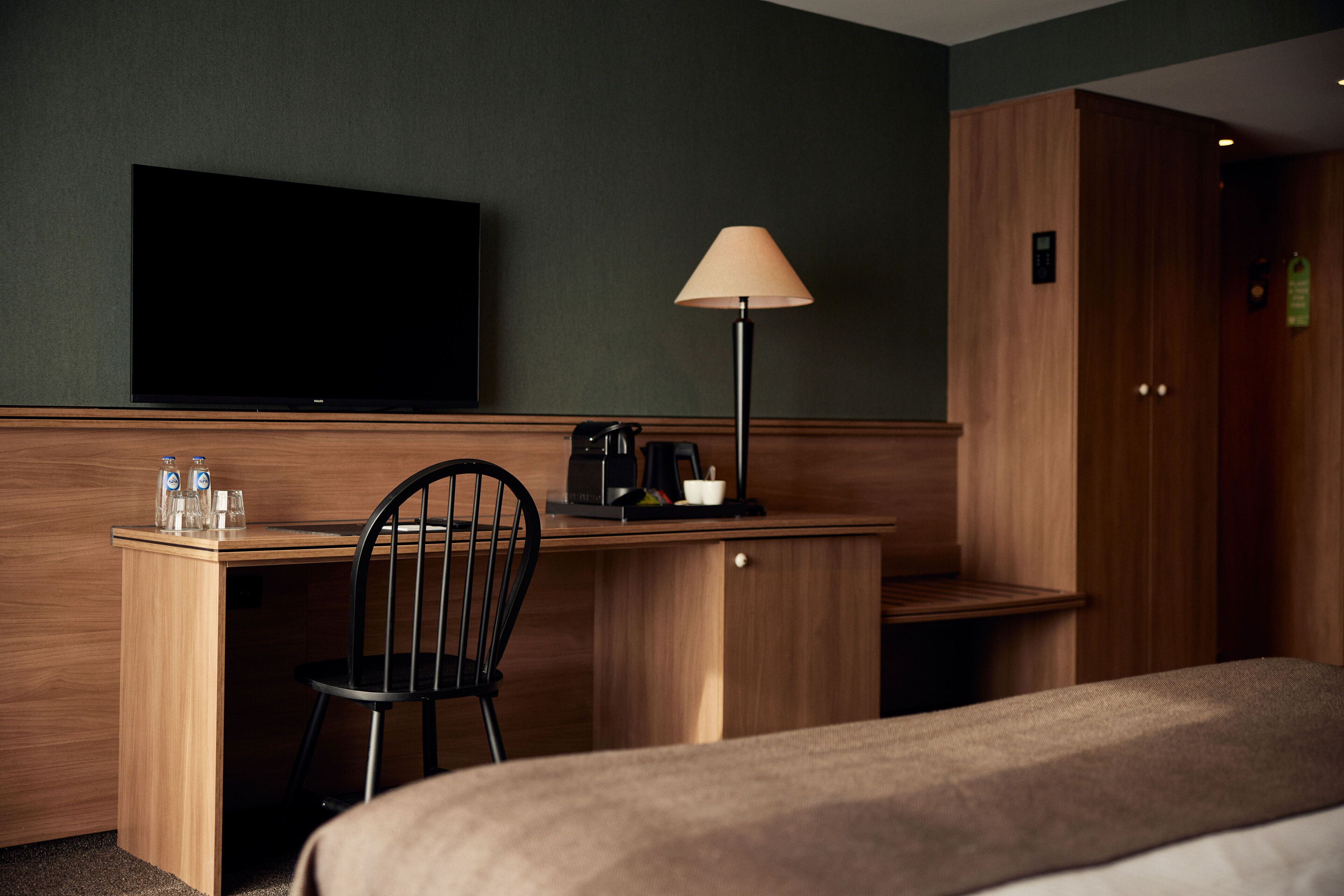 Habitació d'hotel amb escriptori de fusta, una cadira, televisió, làmpada i un llit.