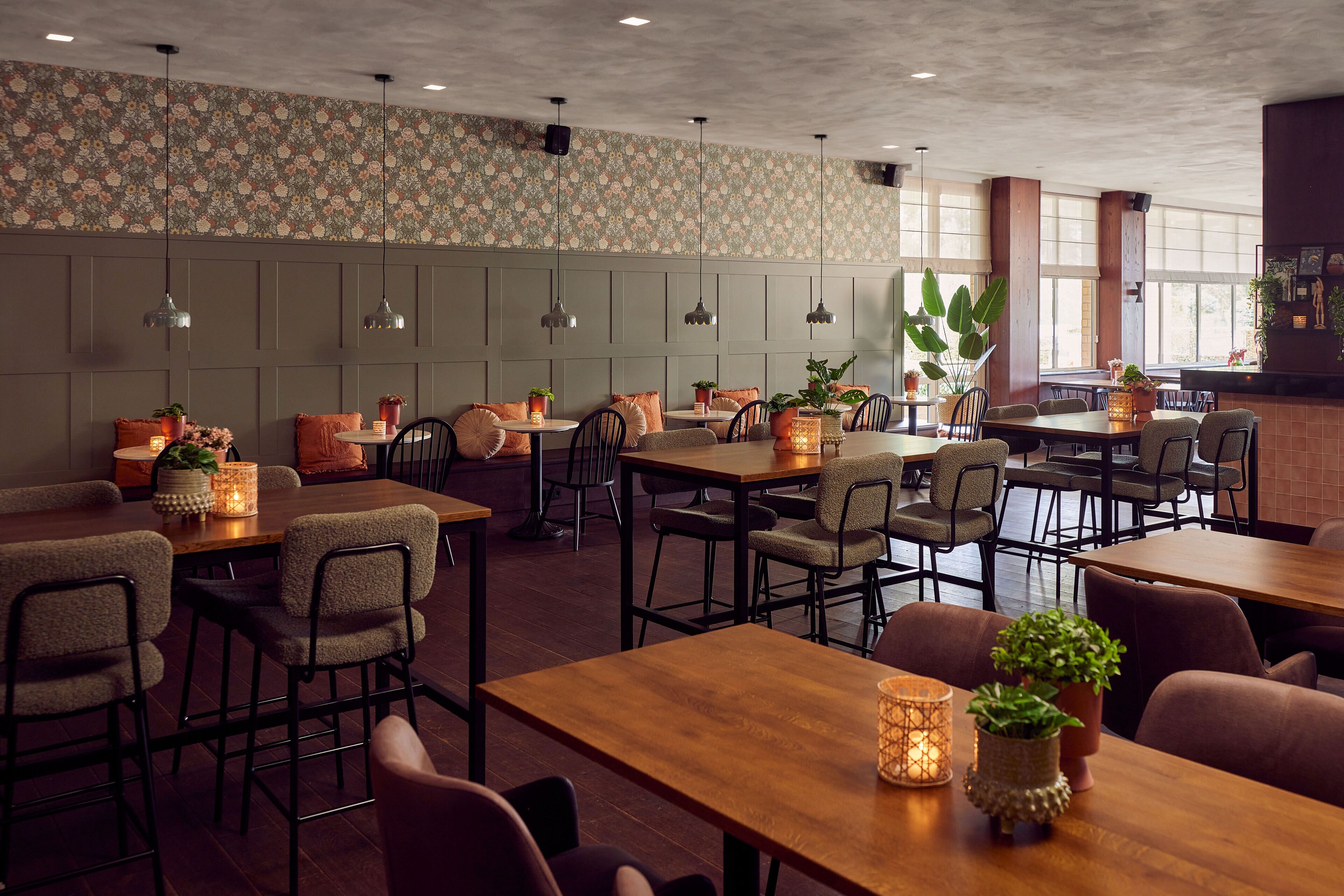 A restaurant with wooden tables and chairs, potted plants, and pendant lighting.