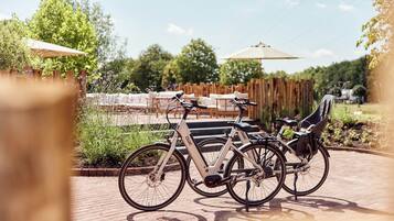 A bicycle parked on a brick pathway with a wooden fence and greenery in the background.