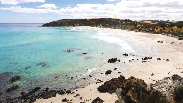 A coastal beach with clear turquoise waters, sandy shore, and rocky outcrops. - Sky House Kangaroo Island (Middle River)