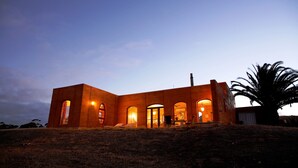 A modern building with multiple arched doorways and large windows, situated on a grassy hill. - Sky House Kangaroo Island (Middle River)