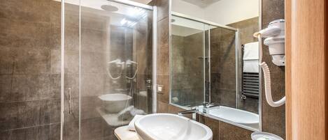 A modern bathroom with a glass shower enclosure, a large white sink, and a mirror reflecting a bathtub.