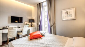 Ein Hotelzimmer mit Bett, Schreibtisch mit Stuhl, Fernseher und einem gerahmten Bild an der Wand.
