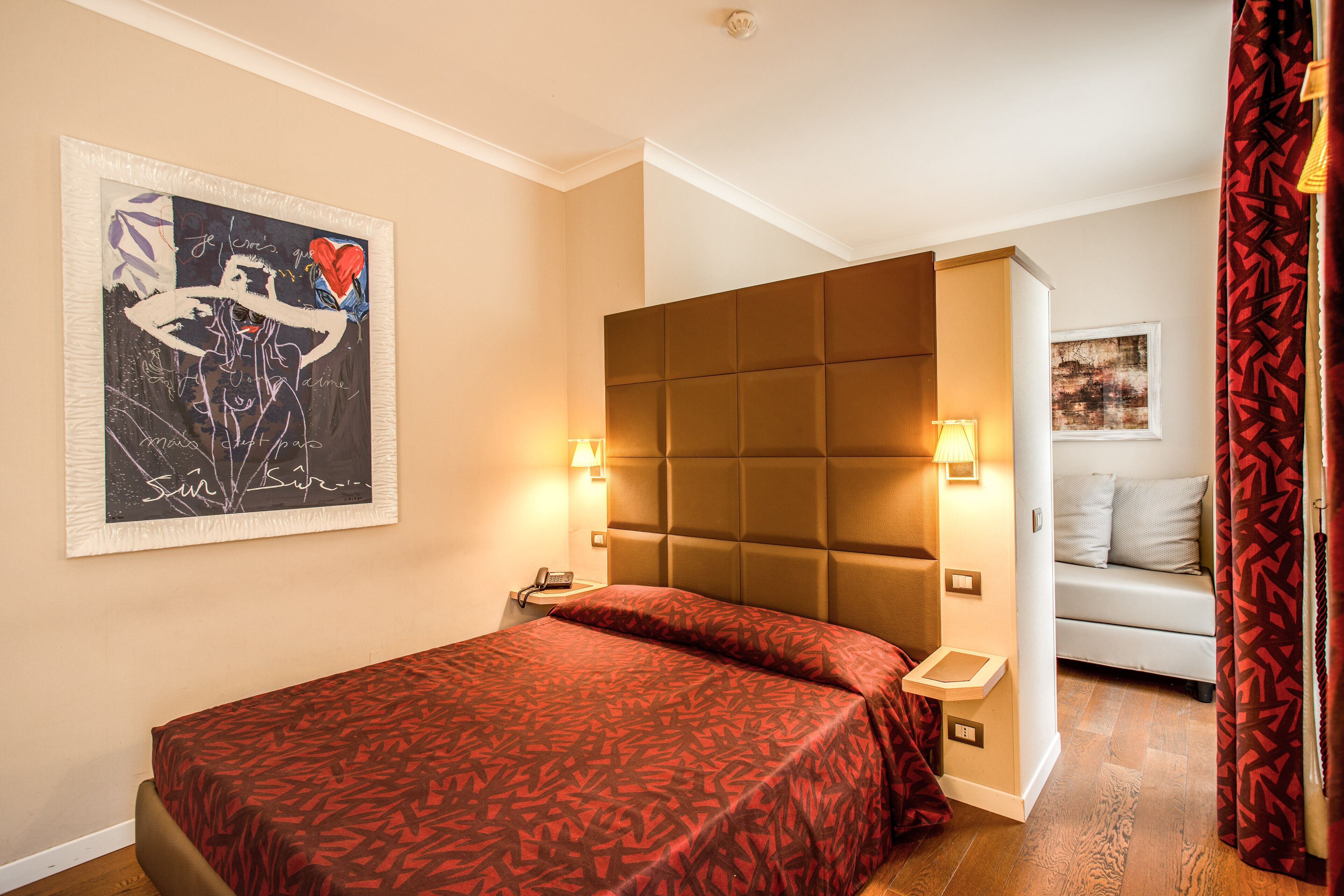 Une chambre d’hôtel avec un grand lit, une tête de lit, des lampes de chevet, un téléphone et un tableau au mur.