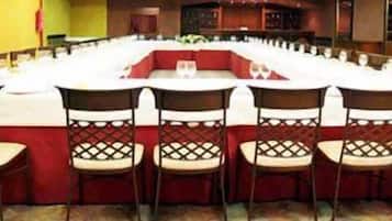 Een vergaderzaal met een lange tafel, rode stoelen en witte tafelkleden.