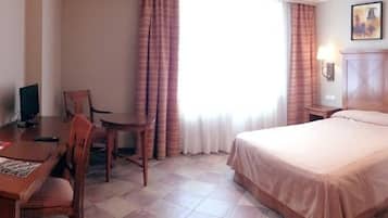 A hotel room with a bed, desk, chair, lamp, and curtains.
