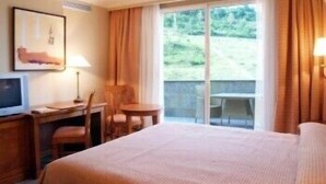 A hotel room with a bed, a desk with a chair, a television, and a window with curtains. - Villava Pamplona (Villava)