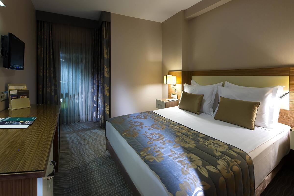 A hotel room with a bed, bedside lamps, a desk, and a television.