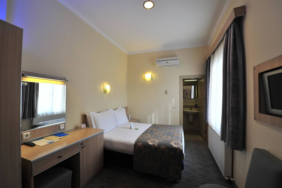 A hotel room with a bed, desk, and a TV mounted on the wall.