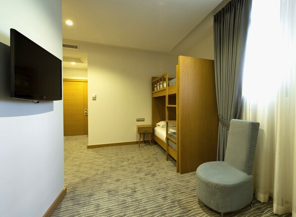 A hotel room with a bunk bed, a television mounted on the wall, a small bedside table, and a chair.