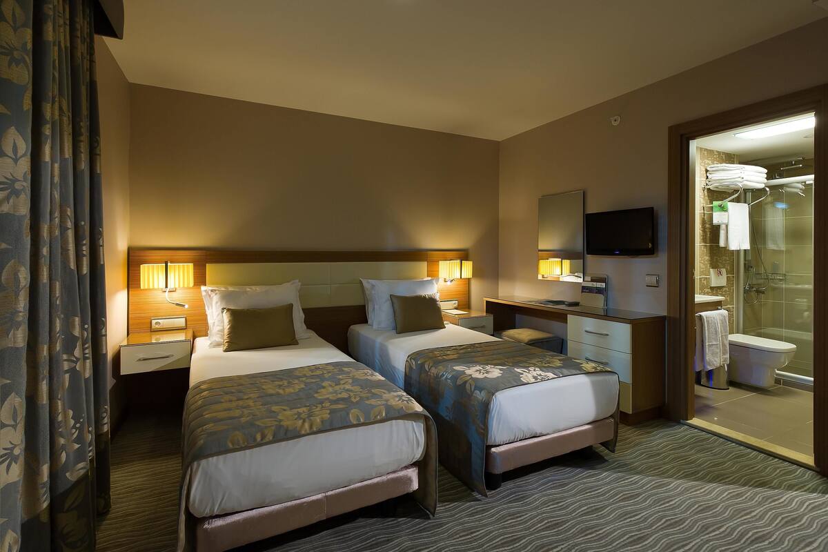 A hotel room with two beds, a desk, a TV, and a bathroom visible through an open door.