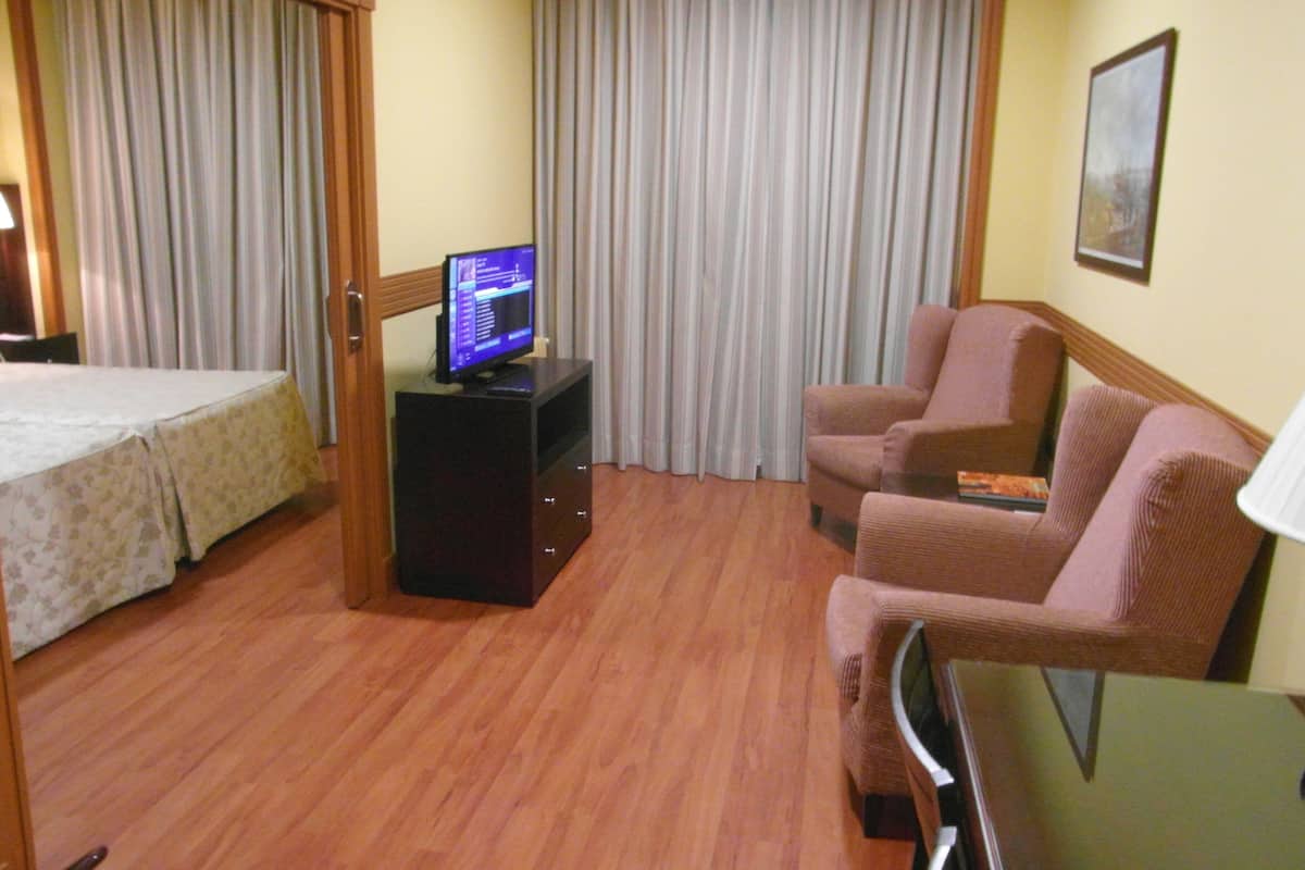 A hotel room with a bed, a television on a stand, a sofa, and a desk.