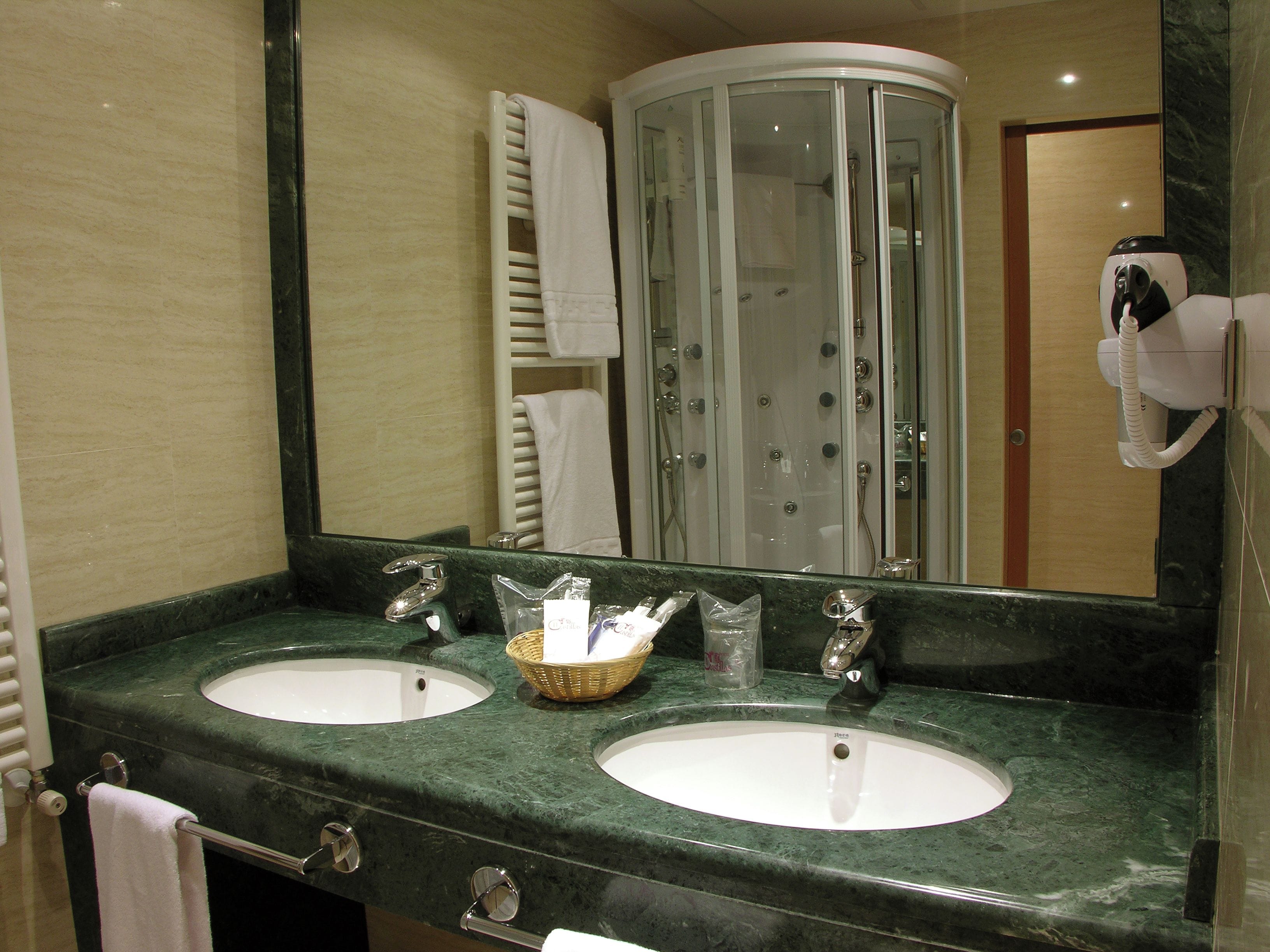 A bathroom with two sinks, a mirror, a towel rack, and a shower enclosure.