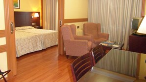 Quarto de hotel com duas camas, uma escrivaninha com cadeira, televisão e janela com cortinas.