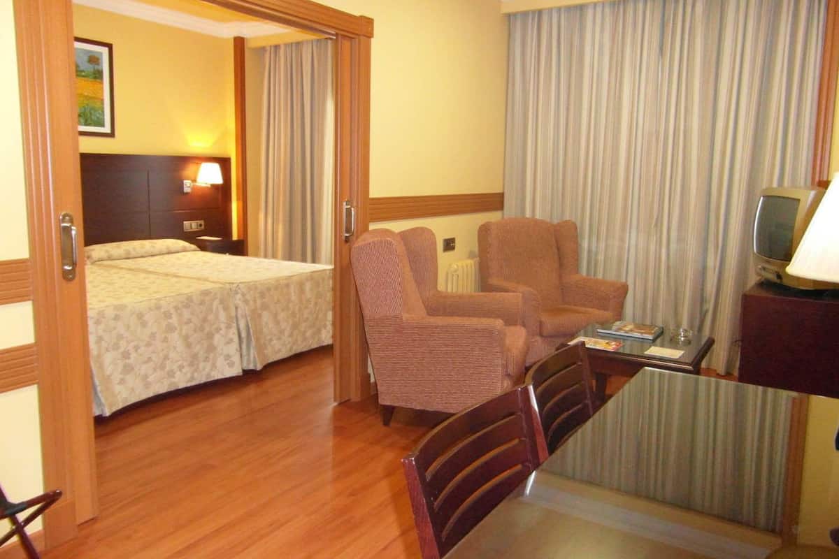 A hotel room with two beds, a desk with a chair, a television, and a window with curtains.