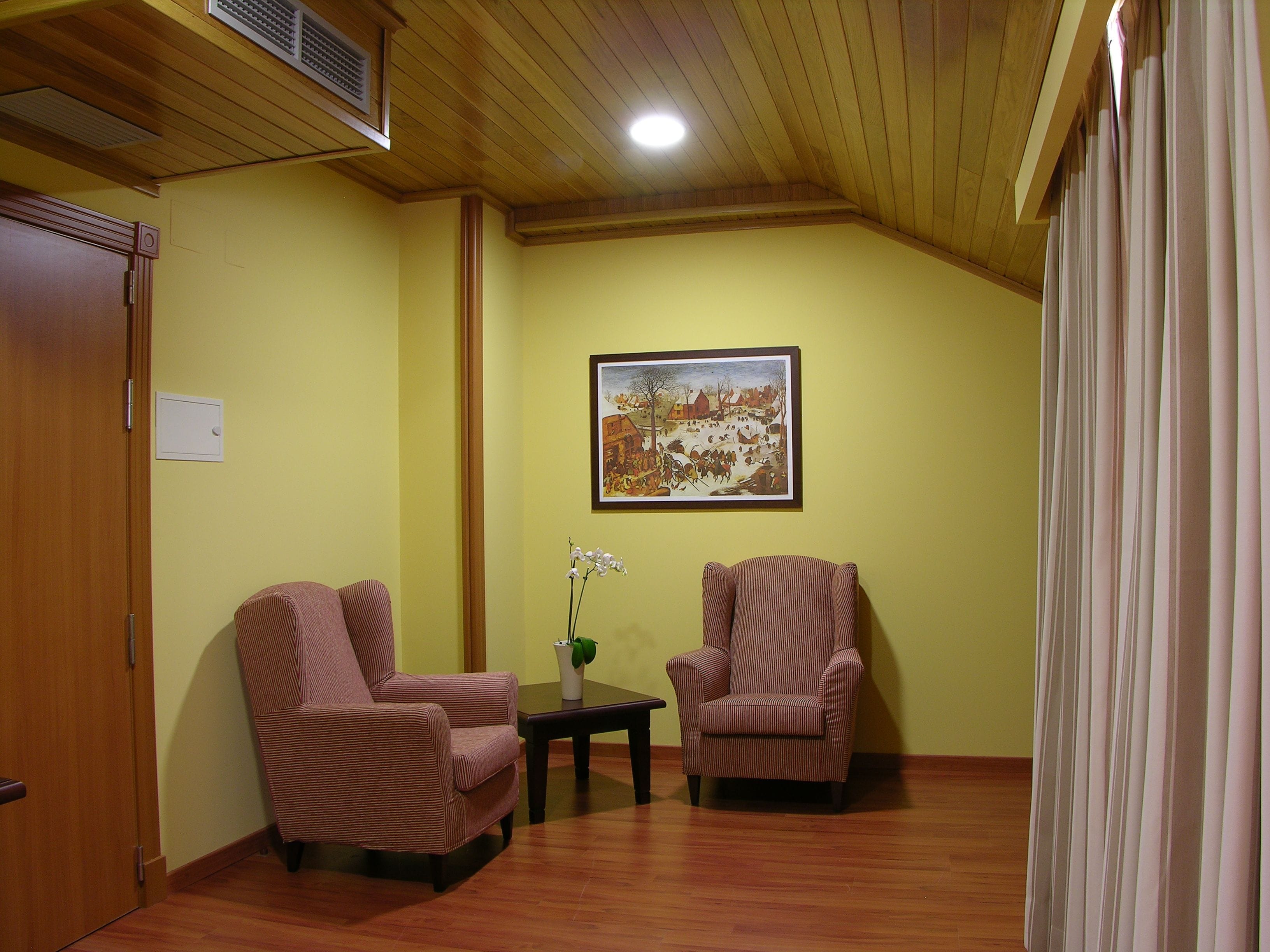 Una habitación con suelo de madera, dos sillones, una mesita, un cuadro en la pared y una puerta.