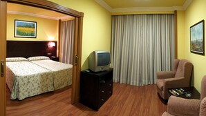 Quarto de hotel com duas camas, uma televisão, uma cadeira e uma pequena mesa.
