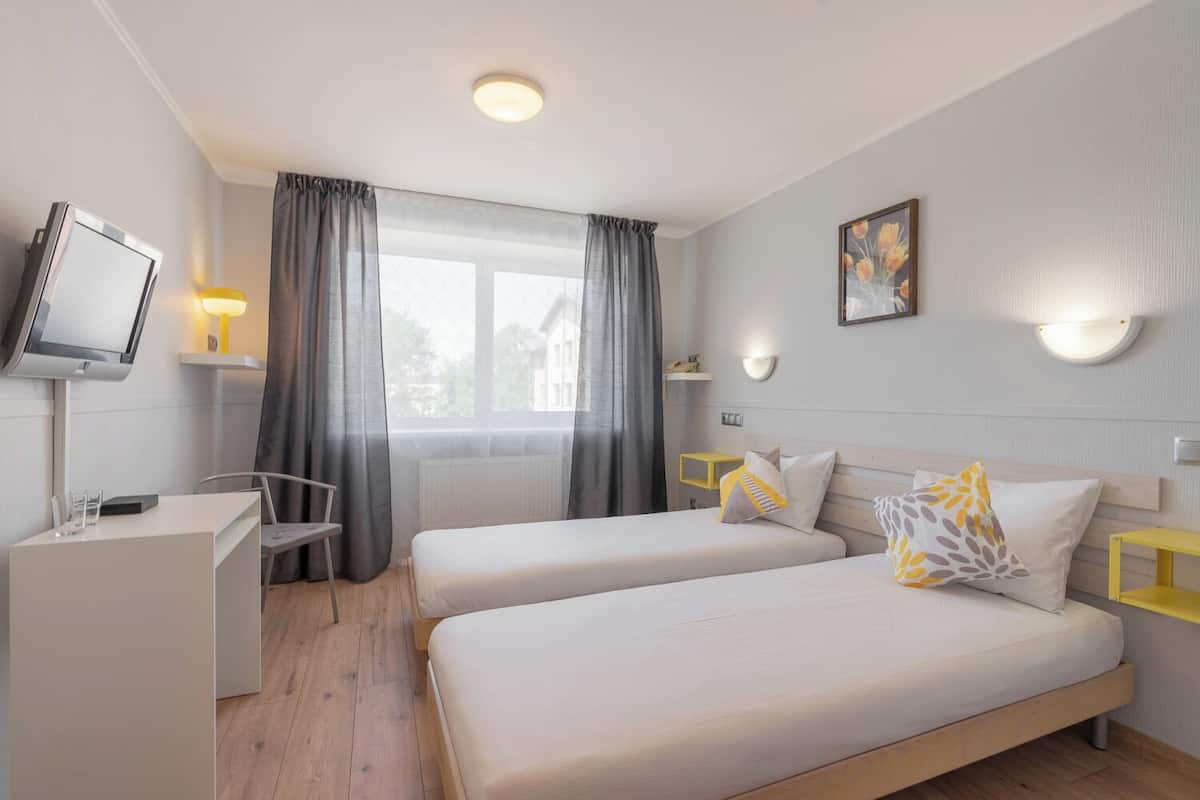 A hotel room with two beds, a desk, a chair, a TV, and a window with curtains.