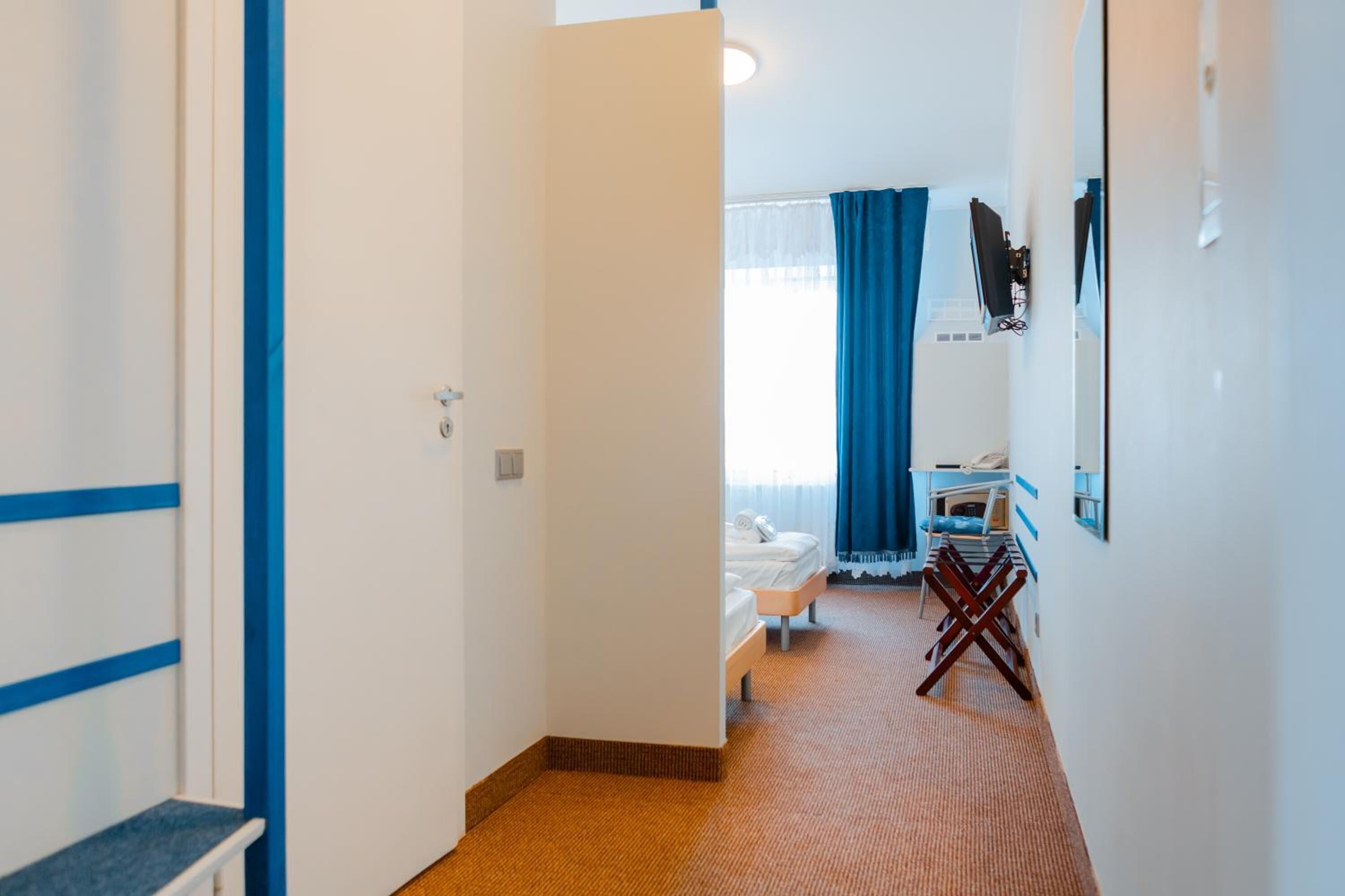 Une chambre d’hôtel avec un lit, un bureau et une chaise. Il y a une fenêtre avec des rideaux et un miroir sur le mur.