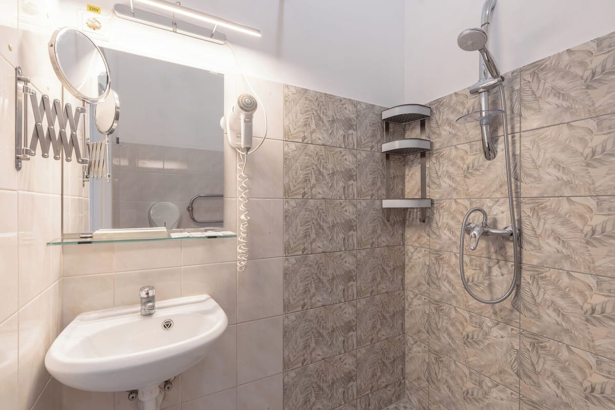 A bathroom with a white sink, a mirror, a hairdryer, and a shower with a handheld showerhead.