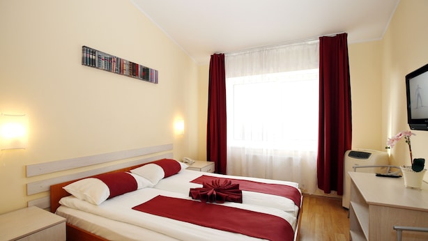A hotel room with two beds, a desk, a chair, a TV, and a window with curtains. - Apart Hotel TOMO (Riga)