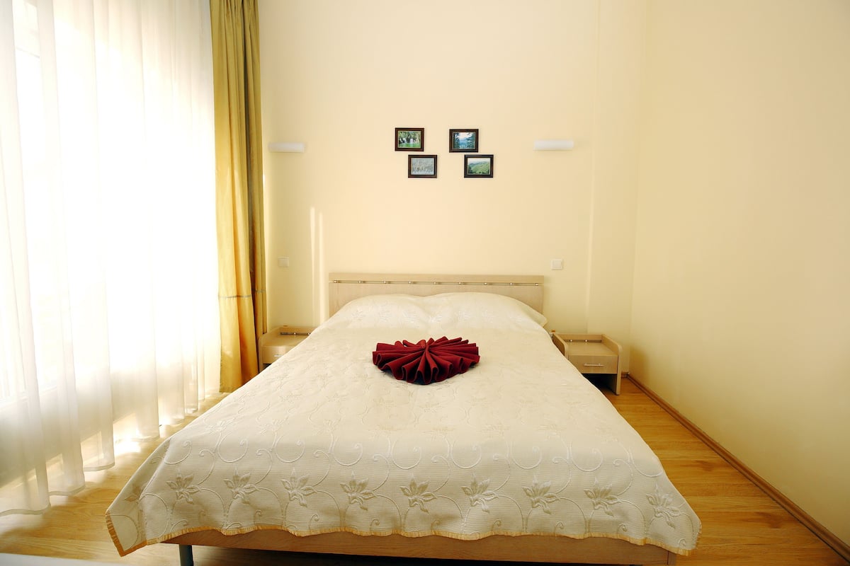 A neatly made bed with a decorative pillow, a bedside table, and a wall with three framed pictures.