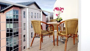 A balcony with wicker chairs and a table, overlooking a building with large windows. - Apart Hotel TOMO (Riga)