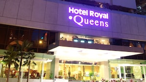 Een hotel met meerdere verdiepingen, met verlichte borden waarop ‘Hotel Royal Queens’ staat.