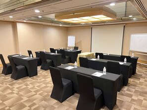A conference room with multiple tables, chairs, and a projector screen. - Hotel Royal Queens (Singapore)