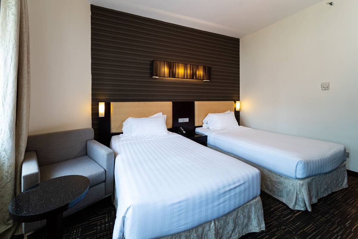 Une chambre d’hôtel avec deux lits, un canapé, une petite table et un luminaire fixé au mur.
