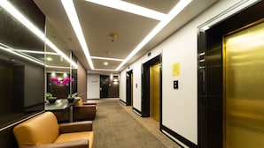 Een hotel lobby met een receptiebalie, een zithoek en liften.