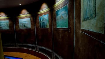 Un pasillo con un sendero iluminado en azul, obras de arte enmarcadas en las paredes y un techo curvo.