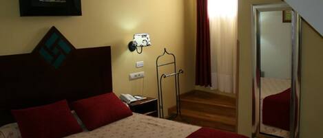 A hotel room with a bed, a bedside table, a mirror, a coat rack, and a staircase leading to another room.